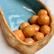 Load image into Gallery viewer, closeup, detail shot of See Pod inspired wall sculpture, stoneware husk like nest of seeds or eggs in light orange with a blue interior