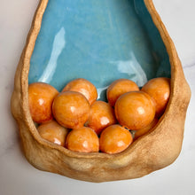 Load image into Gallery viewer, closeup, detail shot of See Pod inspired wall sculpture, stoneware husk like nest of seeds or eggs in light orange with a blue interior