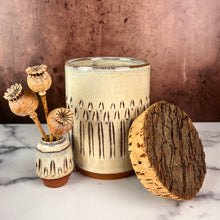 Load image into Gallery viewer, Canister (Medium size) for beautiful display and storage. this canister is wheel thrown from red stoneware clay, carved with a pattern and glazed in a speckled white glaze. the canister has a natural, rough cork lid. shown here with a mini bud vase, sold separately.