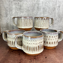 Load image into Gallery viewer, A collection of wheelthrown carved mugs glazed in rustic white glaze. the carved facets show through the white glaze. 
