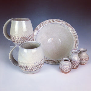 7" stoneware bowl shown with matching mugs tiny bud-vases. all are thrown in a red clay then hand carved, and glazed with a white glaze.