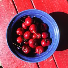 Load image into Gallery viewer, cobalt blue berry colander full of red cherries on a red picnic table, pottery strainer with blue glaze