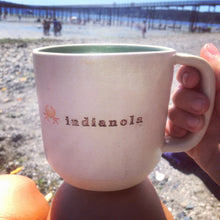 Load image into Gallery viewer, Wheel thrown pottery mug with &quot;indianola&quot; and an image of a crab inset on the outside. white outside, turquoise green glaze interior