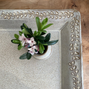 showing the detailed carved edge on a speckled white tray. vine and leaf pattern carved into edge of tray. shown with small matching  bud vase 