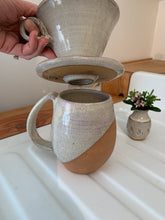 Load image into Gallery viewer, Detail shot of bottom of Coffee pour over and drip edge. wheel-thrown pottery, white glaze with speckled white glaze. shown with matching angle dipped mug and carved bud vase. Fern Street Pottery