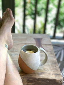 The artist relaxing on her porch with an iced chai and lemon in an angle dipped mug featured in White Speckle. pictured on a handcrafted maple table.Fern Street Pottery. Angle dipped mug.