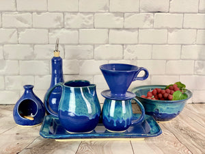 Hand crafted pottery from Fern Street Pottery. Blue world mug, pitcher, tray and colander. Coffee pour over, oil cruet, and salt cellar in cobalt blue.