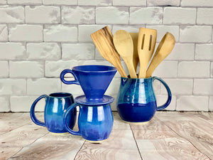 two blue world mugs shown with a blue coffe pour over, and a matching pitcher, used as utensil holder