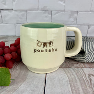 Wheel thrown pottery mug with "poulsbo" and images of marine flags which spell "pbo" inset on the outside. white outside, turquoise green glaze interior