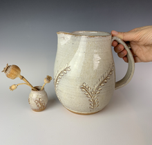 Load image into Gallery viewer, Carved pitcher in speckled white. the red clay and speckled white glaze work well together to show the carved detail. the carved pattern on the vase is reminiscent of vines or growing plants. shown here with a carved bud va