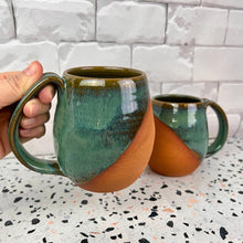 Load image into Gallery viewer, Wheel thrown and hand crafted in red-brown stonware clay, this angle dipped mug is featured in a drippy moss green glaze which shows a lot of color variation.. beautiful color and textures. holds 14-16 oz