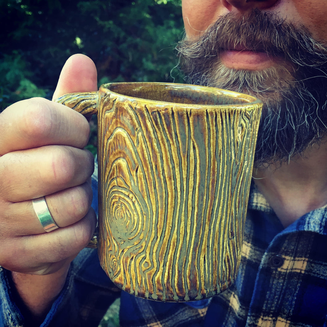 Lumberjack, bearded man drinking out of a pottery mug, carved with woodgrain to imitate tree texture. stoneware, Fern Street Pottery.