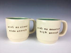 set of customized text mugs. mugs read : ain't no river wide enough / ain't no mountain high enough. white mugs, brown text, turquoise interior