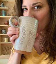 Load image into Gallery viewer, The artist drinking from her travel mug. wheel thrown in red clay, carved, white glaze. finger loop handle so it fits in cupholder