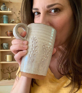 The artist drinking from her travel mug. wheel thrown in red clay, carved, white glaze. finger loop handle so it fits in cupholder