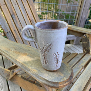 tall latte size travel mug with finger loop handle. vine carvings and white glaze. shown on adirondak chair