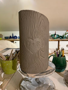 woodgrain textured vase, cylindrical in shape with heart and initials carved into texture. reminiscent of a tree with carved initials