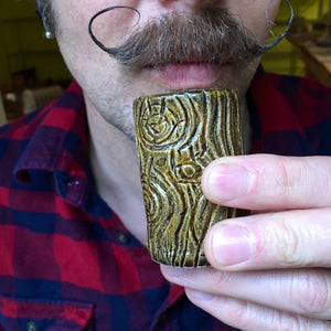 mustachioed man with handlebar mustache drinking from a lumberjack shot glass. pottery shot glass carved to look like wood