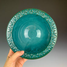 Load image into Gallery viewer, the artist holding a stoneware bowl with a hand carved rim. This bowl is glazed in teal