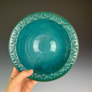 the artist holding a stoneware bowl with a hand carved rim. This bowl is glazed in teal
