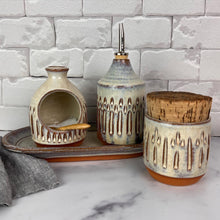 Load image into Gallery viewer, Canister for beautiful display and storage. this canister is made from red stoneware clay, carved with a pattern and glazed in a speckled white glaze. the canister has a natural, rough cork lid. approximately 3.5 inches wide and 3.5 inches tall. shown here with the olive oil cruet, salt cellar and tray (set sold separately)