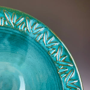 close up detail of the carved rim of a bowl. the red clay shows through the teal glaze at the edges of the carved lines.