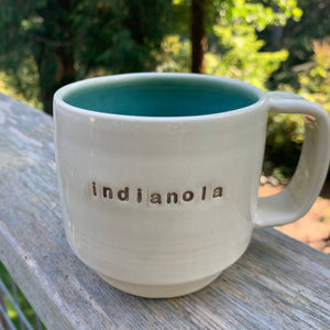 indianola mug, wheelthrown with the word indianola inset. white exterior, glossy turquoise interior