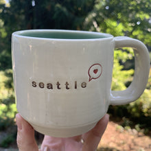 Load image into Gallery viewer, seattle &quot;love&quot; mug, wheelthrown with heart in speech bubble image and the word seattle inset. white exterior, glossy turquoise interior