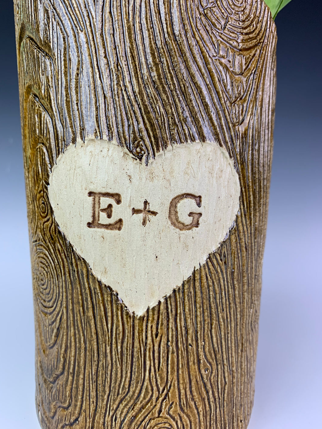 close up detail texture shot of a woodgrain, lumberjack vase. the vase has a heart and initials carved into the wood-like surface