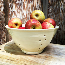 Load image into Gallery viewer, large pottery colander in pure white glaze, shown full of apples, rustic wood background