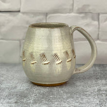 Load image into Gallery viewer, a wheel thrown and hand carved mug sits in a kitchen setting. the mug is thrownin red stoneware which shows throught the white glaze at the edges of the mug. the mug has a repeated line pattern scratched pattern carved into it.